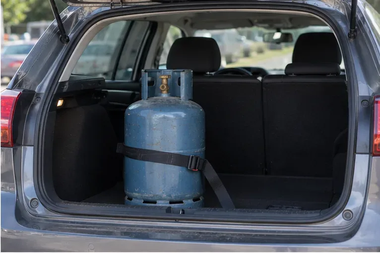Une bouteille de gaz maintenue debout et sanglée dans le coffre d'une voiture pour éviter qu'elle ne se déplace.