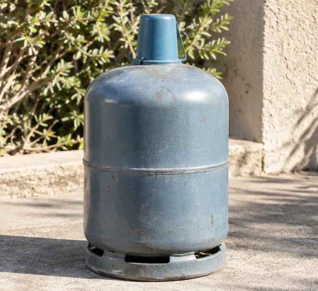 Bouteille de gaz métallique usagée posée debout à l’extérieur, avec son chapeau de protection visible