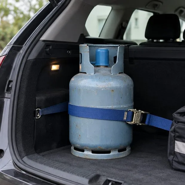 Une bouteille domestique de gaz, robinet protégé, est maintenue debout par une sangle dans le coffre d’un véhicule