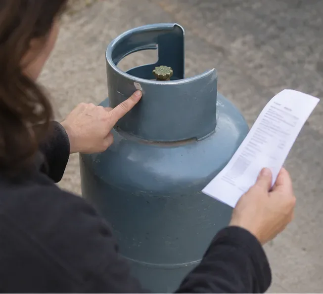Personne examinant les marquages près du robinet d’une bouteille de gaz tout en tenant un document