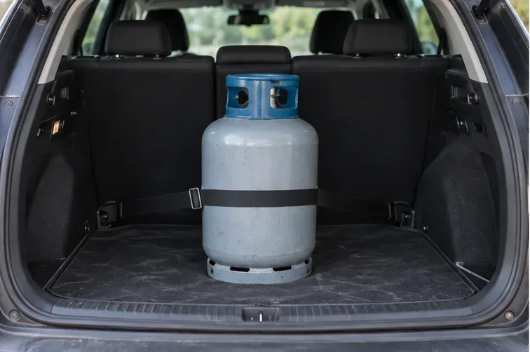 Une bouteille de gaz domestique est immobilisée par une sangle dans le coffre d’un véhicule stationné, pour éviter qu’elle ne roule pendant le trajet.