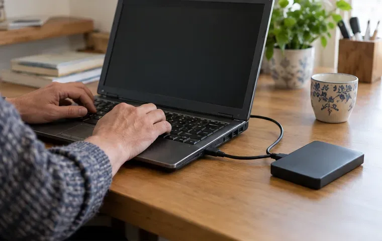 Une personne utilise un ancien ordinateur portable relié à un disque externe sur une table en bois.