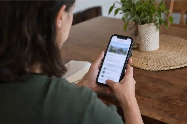 Moradora consulta em um smartphone uma página de informações de descarte, com a tela propositalmente desfocada e sem texto legível.