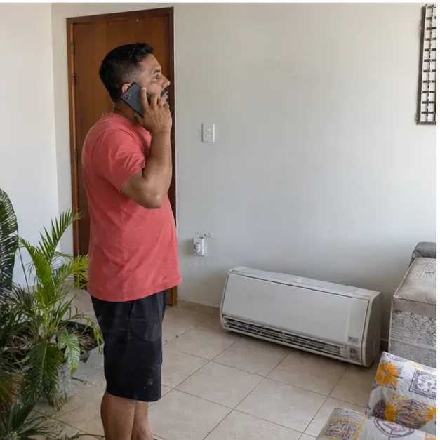 Morador fala ao telefone dentro de casa ao lado de um ar-condicionado retirado e apoiado no piso
