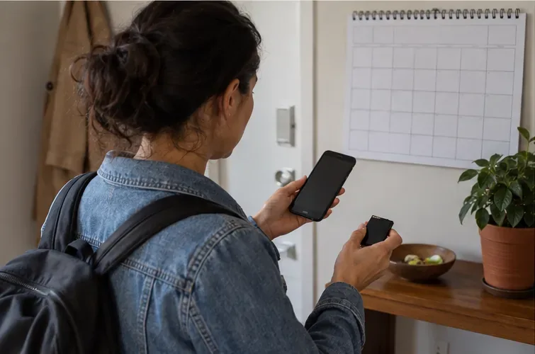 Uma moradora consulta um calendário e um celular em casa antes de sair com uma bateria separada para descarte.