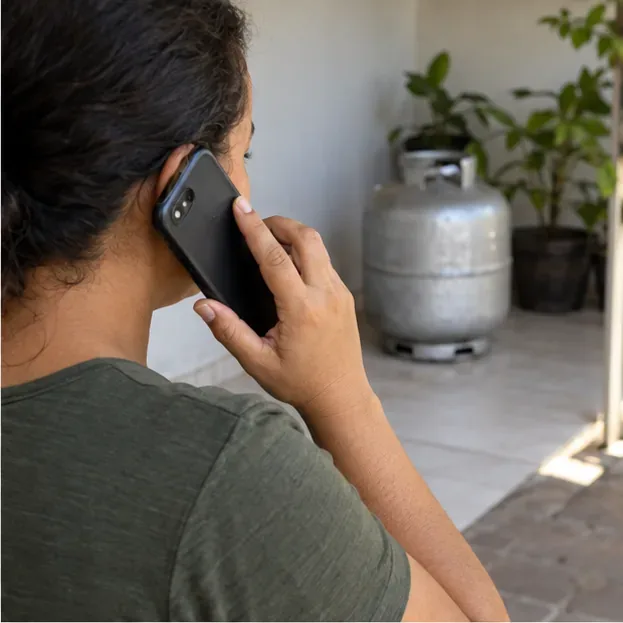 Pessoa telefona para uma revenda de gás enquanto um botijão permanece ao fundo em área ventilada