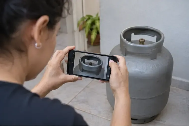 Pessoa usando o celular para registrar a parte superior de um botijão de gás antes de consultar a revenda
