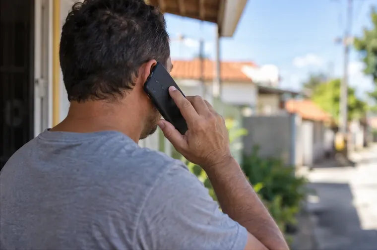 Homem faz uma ligação telefônica em área residencial para confirmar o recebimento de um botijão de gás usado