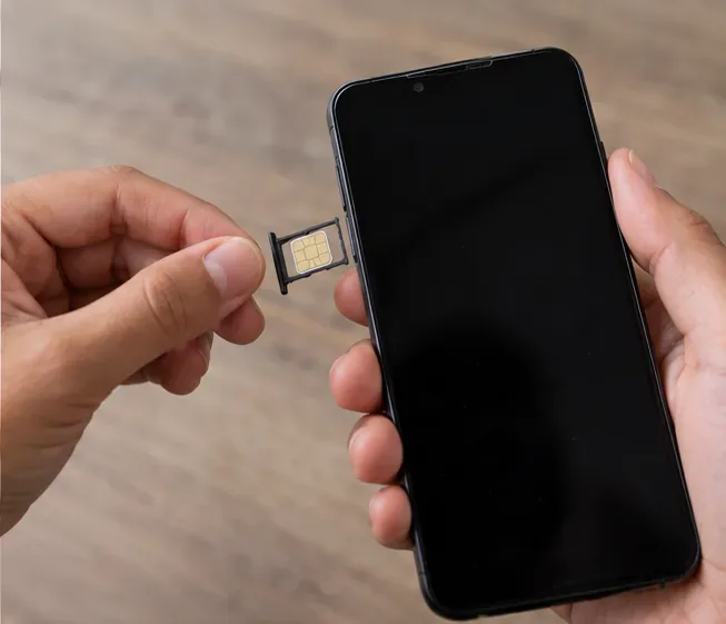 Mãos retirando a bandeja com chip SIM de um smartphone desligado