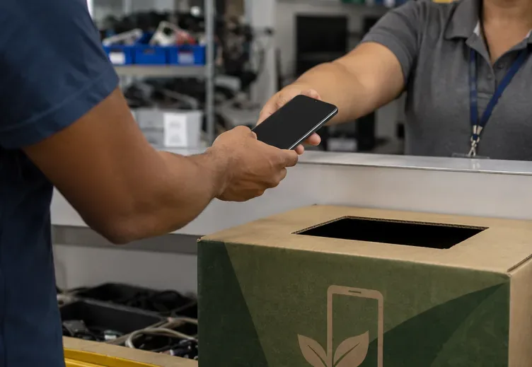 Pessoa entrega um celular a um atendente ao lado de uma caixa para eletrônicos