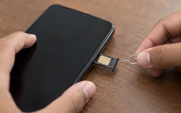 Bandeja com chip parcialmente retirada de um celular desligado sobre uma mesa