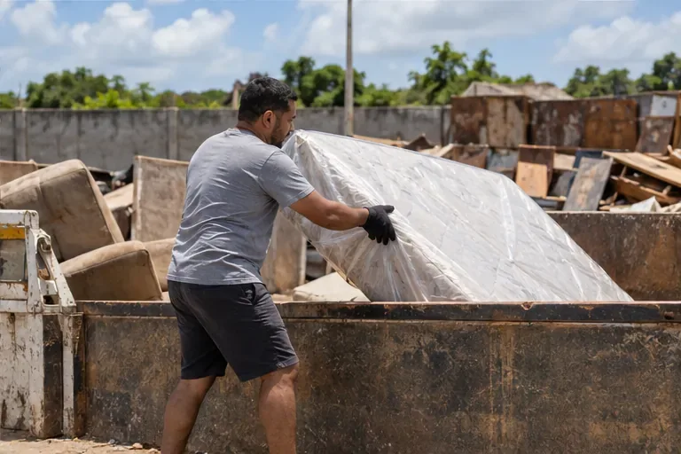 Morador conduz um colchão embalado até uma área genérica de recebimento de resíduos volumosos