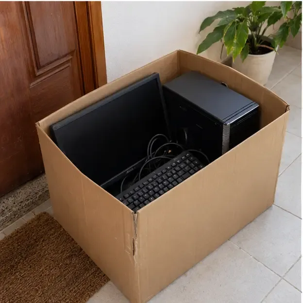 Computador de mesa, monitor, teclado e cabos organizados em uma caixa de papelão perto da porta