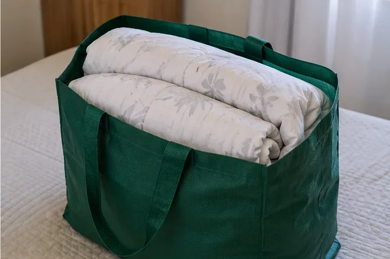 Edredom claro dobrado e acomodado dentro de uma bolsa reutilizável verde