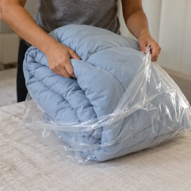 Mãos dobram um edredom azul seco e o colocam dentro de um saco plástico limpo.
