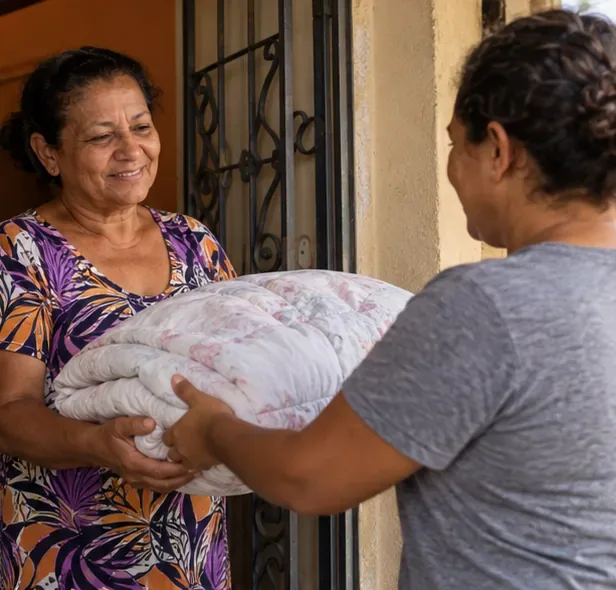 Uma mulher entrega um edredom dobrado a outra pessoa na entrada de uma casa.