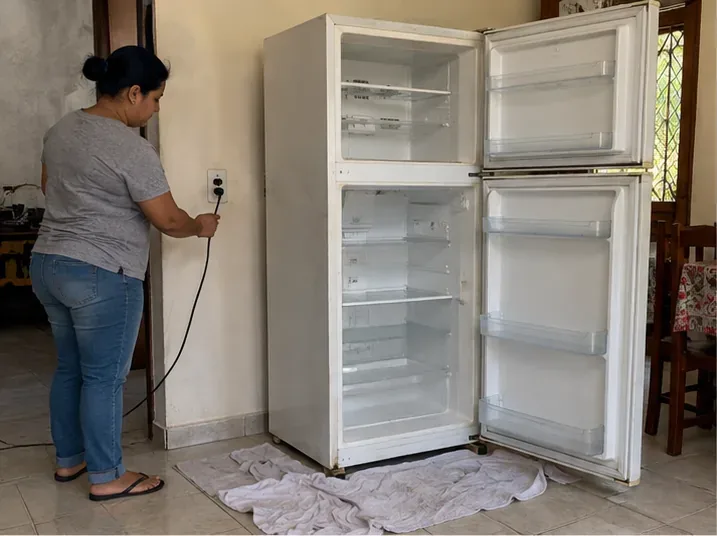 Pessoa retirando o plugue de uma geladeira vazia e aberta antes do transporte para descarte em Belém