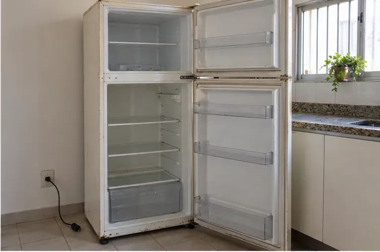 Geladeira antiga vazia, com portas abertas e plugue fora da tomada, pronta para ser movimentada