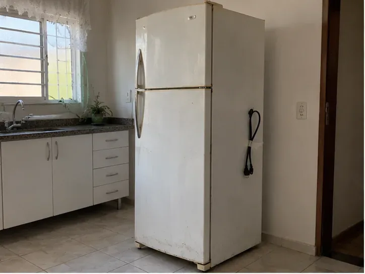 Geladeira antiga desligada dentro de uma cozinha, pronta para ser retirada para descarte correto