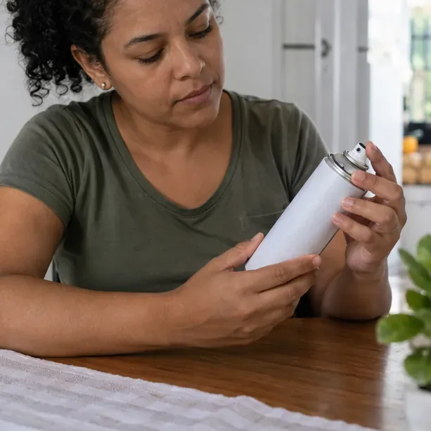 Pessoa examinando uma lata de spray sobre uma mesa, com atenção ao bico e ao rótulo
