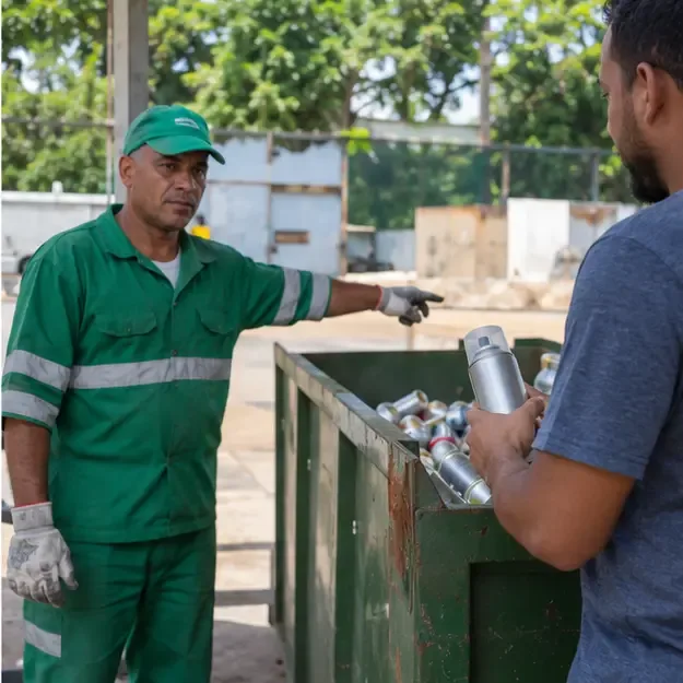 Funcionário de um ponto de recebimento indica um contêiner metálico enquanto outra pessoa segura uma lata de spray intacta.