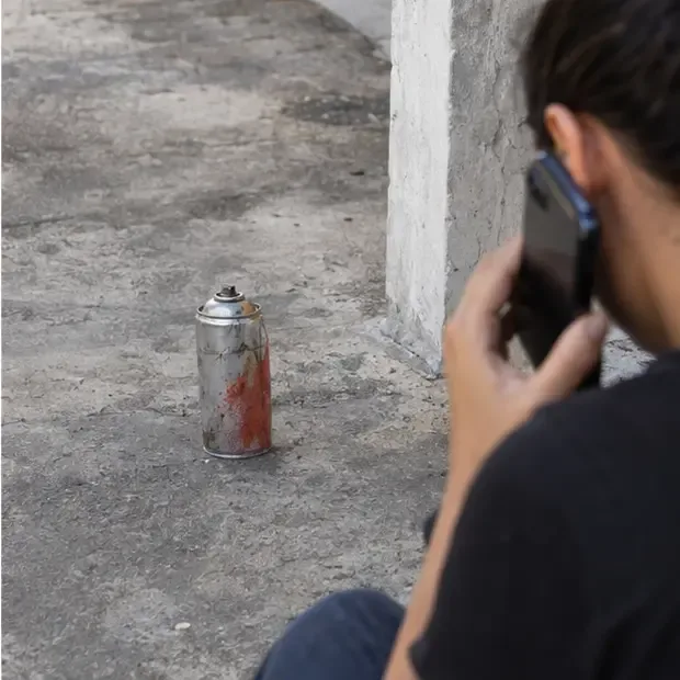 Lata de spray enferrujada e danificada isolada no chão, enquanto uma pessoa usa o telefone sem tocá-la