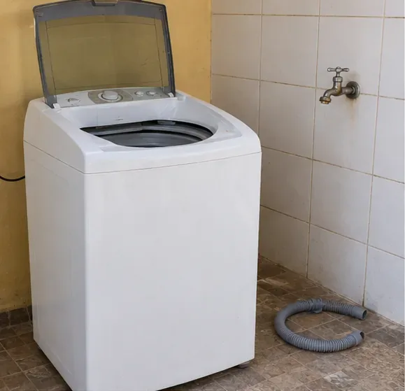 Máquina de lavar vazia com a mangueira de drenagem separada ao lado, em uma área de serviço