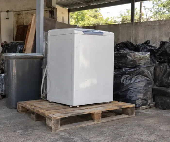 Máquina de lavar mantida na vertical, sobre um pallet e sob cobertura, separada de sacos de resíduos até a retirada.