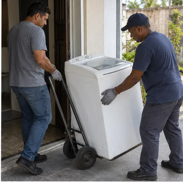 Duas pessoas movimentando uma máquina de lavar em um carrinho de carga pela porta de uma residência.