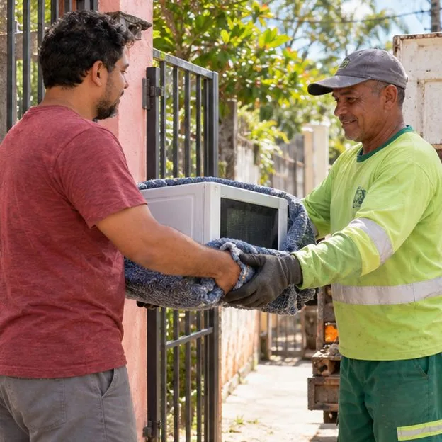 Um morador entrega um micro-ondas a um trabalhador de coleta no portão de uma residência