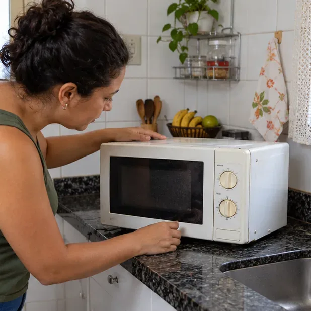 Pessoa observa um micro-ondas antigo e desligado sobre a bancada da cozinha antes de decidir como descartá-lo