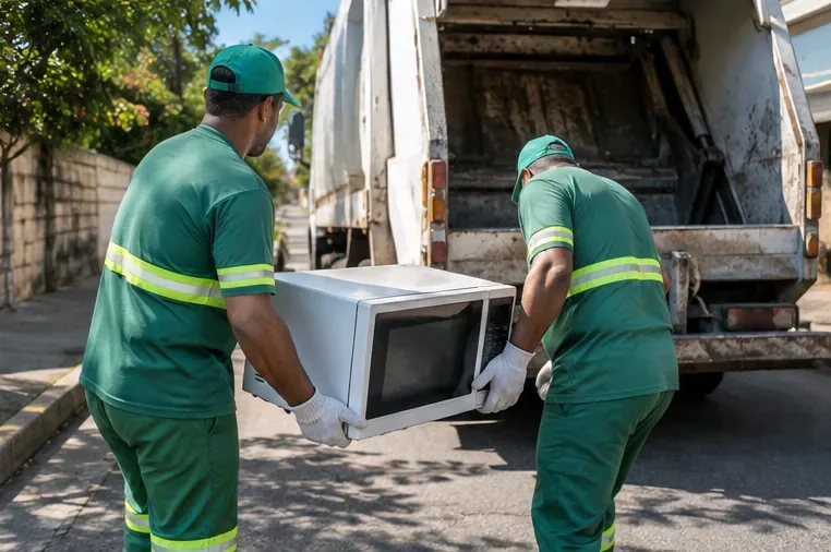 Dois trabalhadores transportando um micro-ondas inteiro até um veículo de coleta
