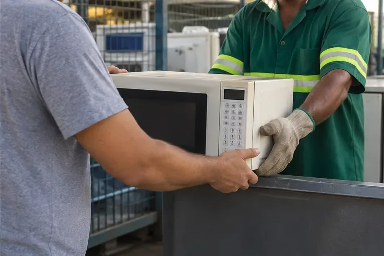 Entrega de um micro-ondas a um trabalhador em área de recebimento de eletroeletrônicos