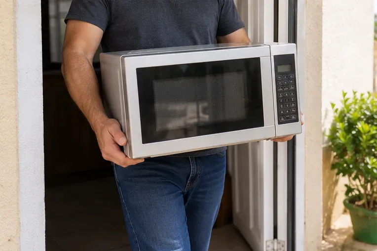 Pessoa carregando um micro-ondas com as duas mãos pela base ao sair de casa