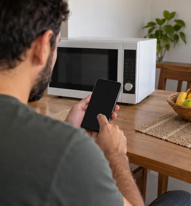 Pessoa segura celular de tela escura diante de um micro-ondas sobre a mesa