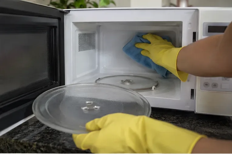 Mãos com luvas retirando o prato de vidro e limpando o interior de um micro-ondas