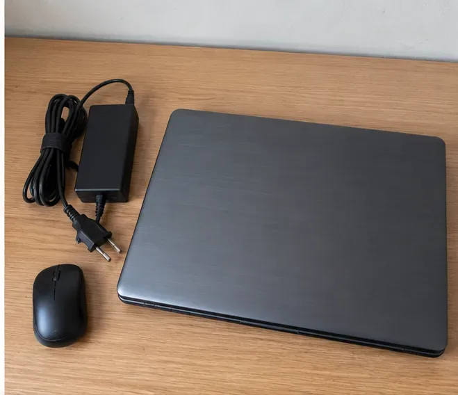 Notebook desligado ao lado de carregador e mouse separados sobre uma mesa