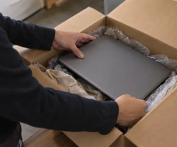 Notebook fechado é protegido com material macio dentro de uma caixa de papelão para transporte