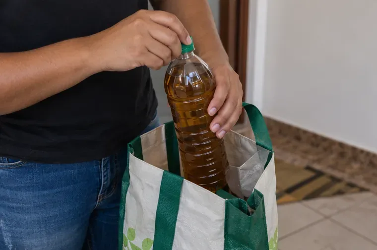 Pessoa fechando uma garrafa PET com óleo usado e colocando-a em uma sacola reutilizável