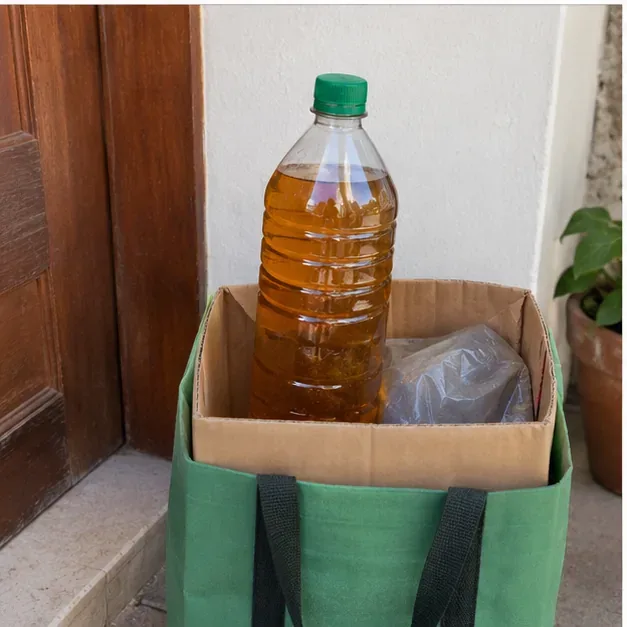 Garrafa plástica com óleo de cozinha usado, fechada com tampa de rosca e mantida em pé dentro de uma caixa para transporte.