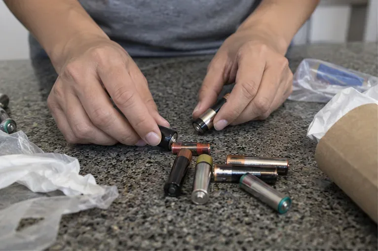 Pessoa separando pilhas AA e AAA usadas sobre uma bancada antes de armazená-las para descarte