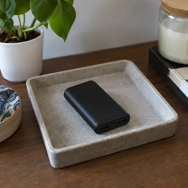 Power bank desligado e separado de objetos metálicos em uma bandeja seca sobre uma mesa.