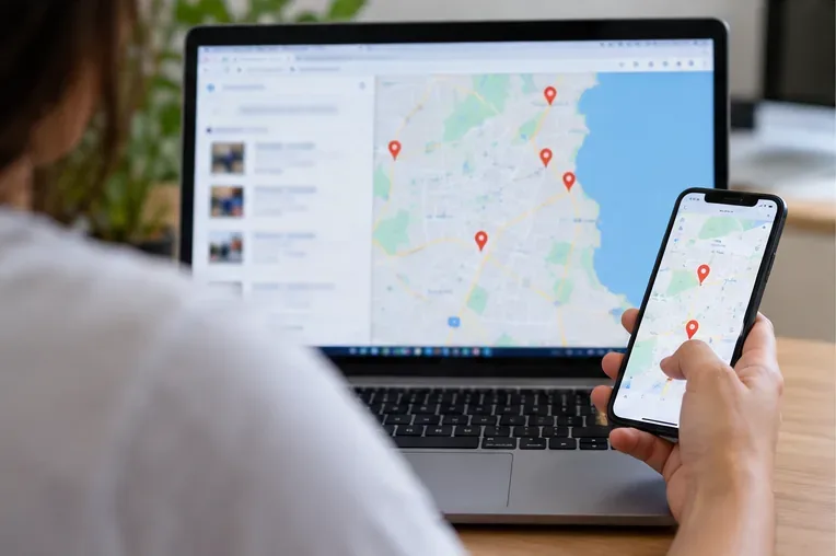 Pessoa consultando um mapa com marcadores em um celular e um notebook para localizar um ponto de entrega