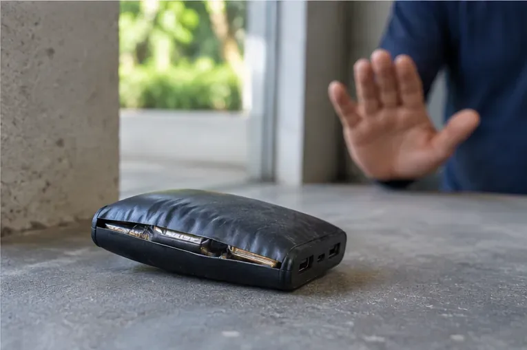 Power bank bastante inchado e com a carcaça aberta pela deformação, enquanto uma pessoa mantém a mão afastada