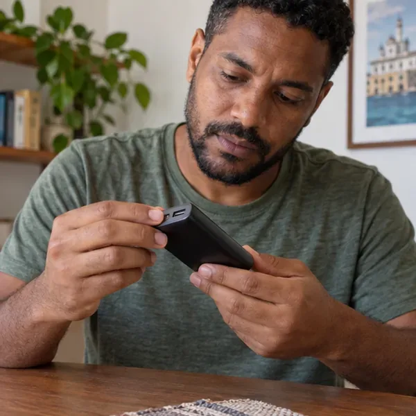 Pessoa examinando um power bank preto desligado sobre uma mesa