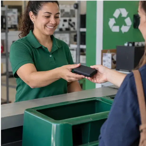 Pessoa entregando um power bank a um atendente em um ponto de recebimento de materiais recicláveis