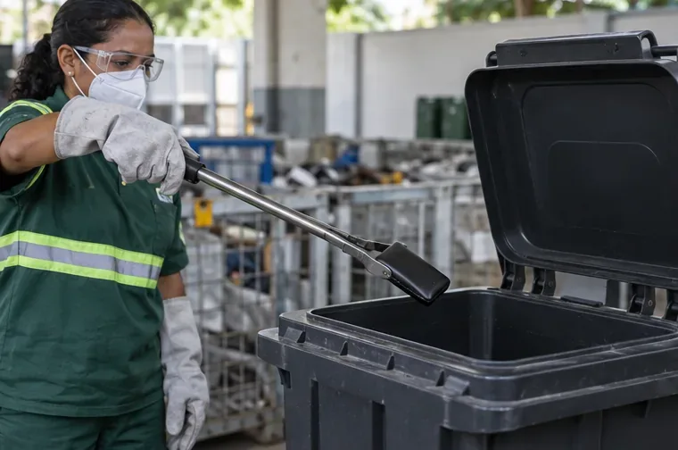 Profissional de reciclagem usa ferramenta de cabo longo para colocar um power bank danificado em um recipiente rígido com tampa