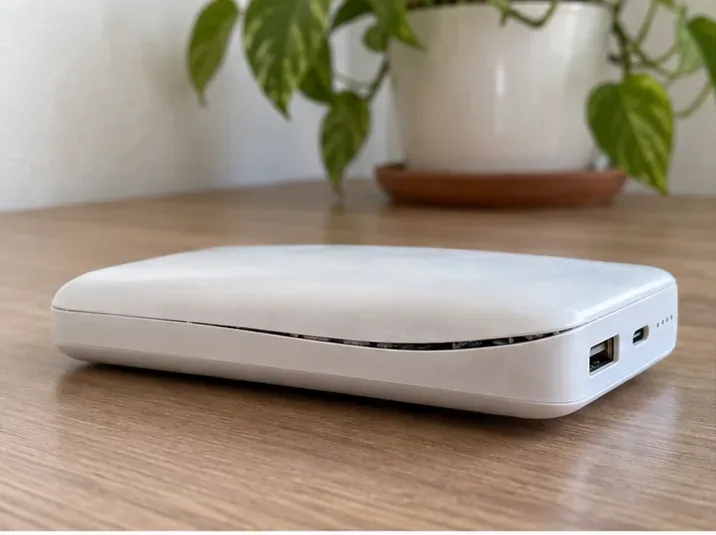 Power bank branco com a carcaça levantada e uma abertura visível na emenda, sobre uma mesa