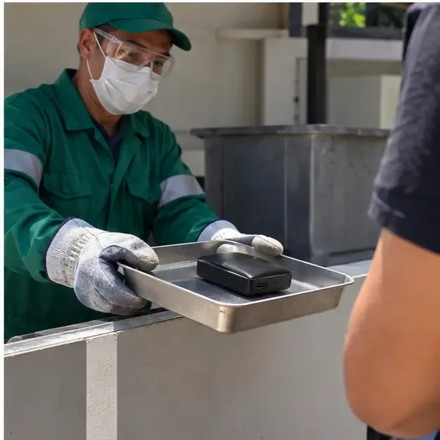 Profissional protegido recebe um power bank estufado em uma bandeja rígida em uma área de triagem de resíduos