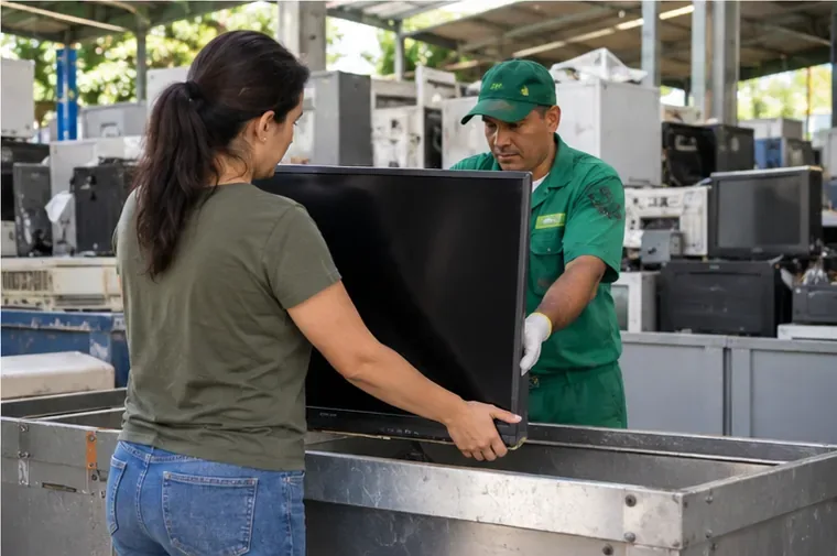 Pessoa entregando uma televisão a trabalhador em área de recebimento e triagem de equipamentos eletrônicos